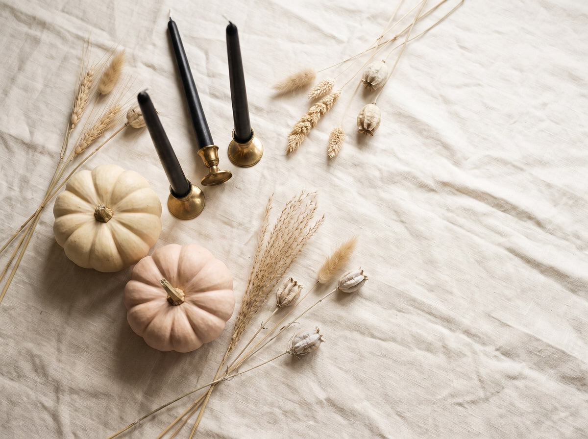 Pale heirloom pumpkins, black taper candles and dried botanical stems on cream linen.
