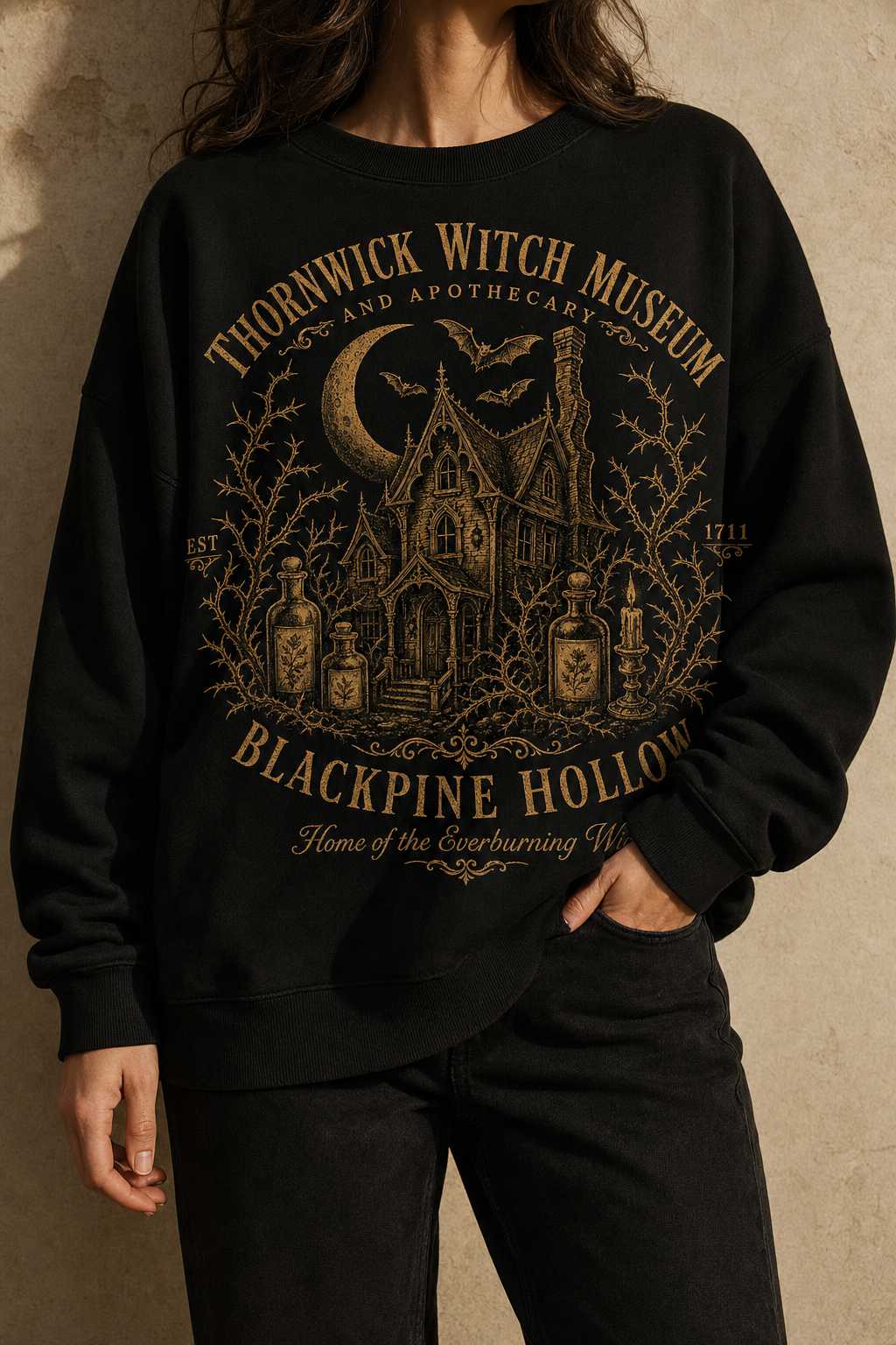 Woman wearing the Thornwick Witch Museum black crewneck against a cream wall