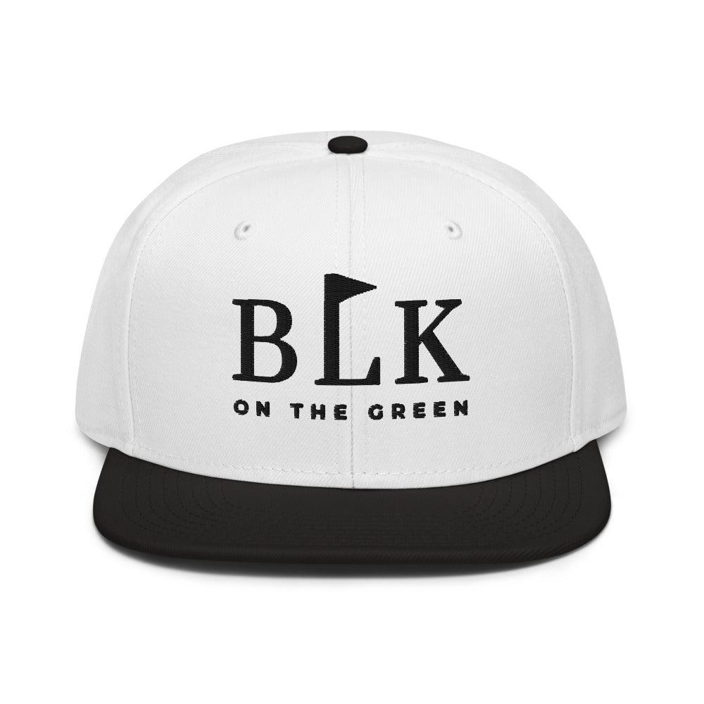The Tee Box Snapback with a white crown and black brim, BLK on the Green embroidered in black